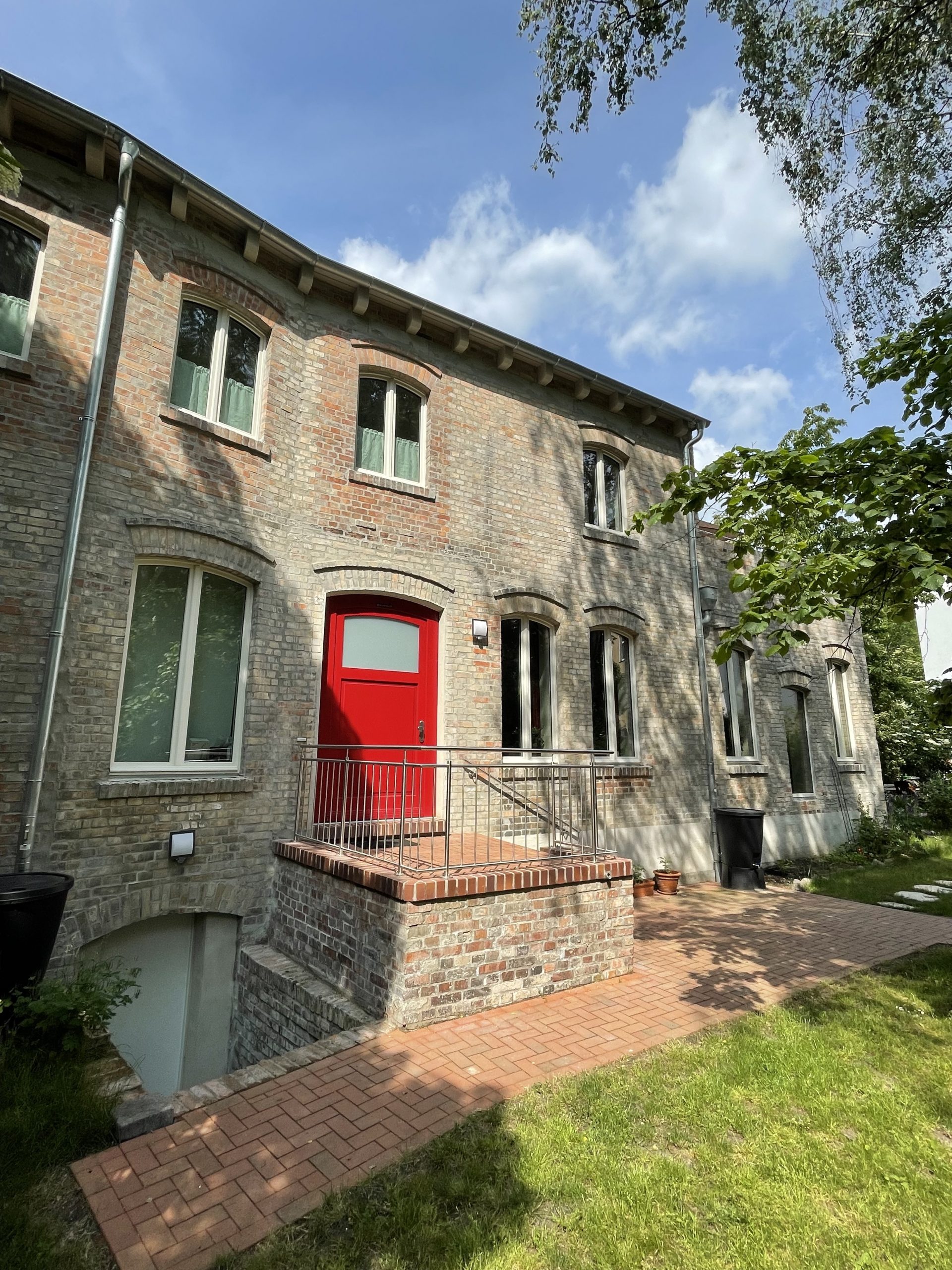 Fotografie der steinernen Eingangstreppe und der roten Eingangstür des Hinterhauses im Glauchaviertel vom Garten aus mit grünen Zweigen im Vordergrund