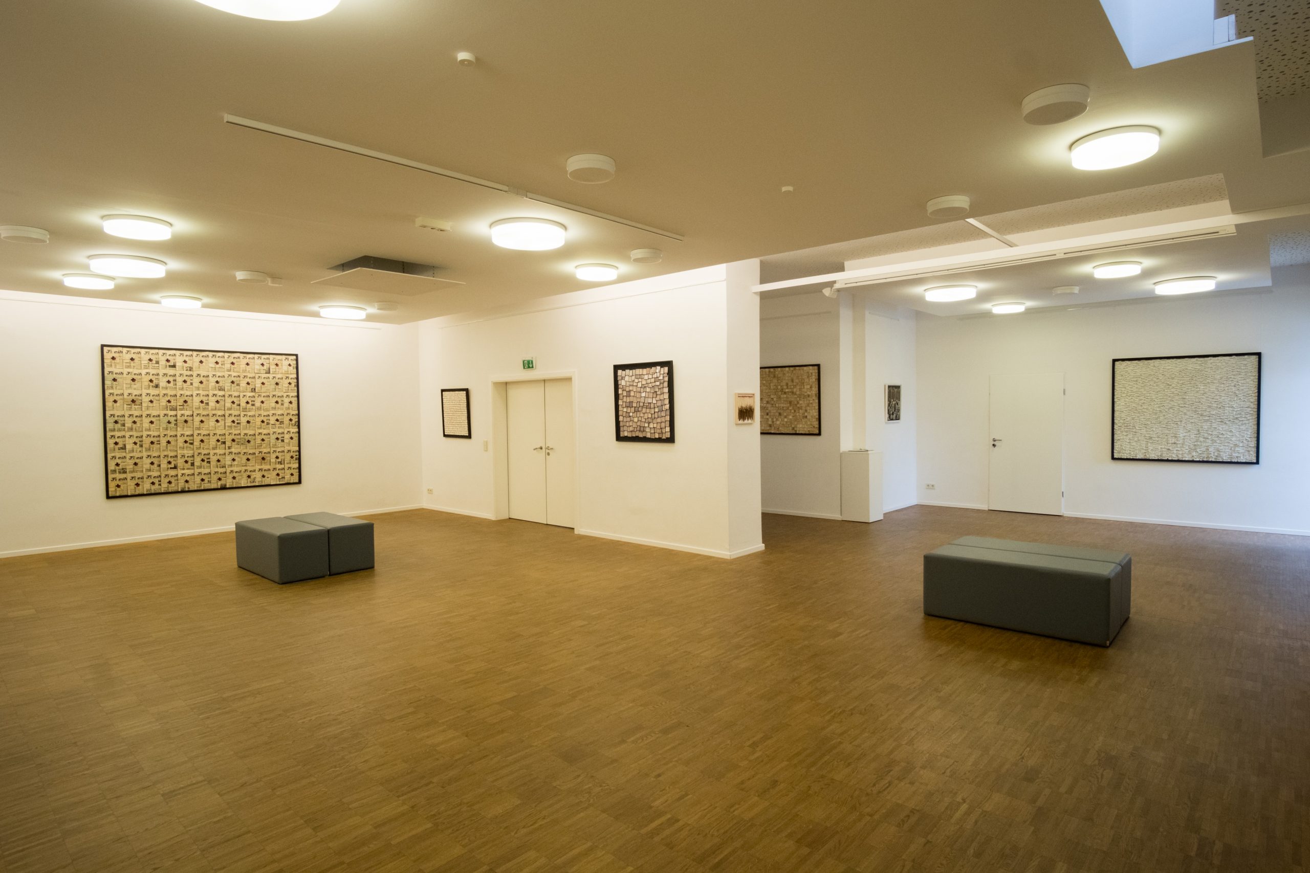 Galerie im ersten Obergeschoss des Lichthauses. Kunstwerke sind auf weißen Wänden platziert, zwei Doppelsitzbänke stehen auf dem Stäbchenparkettboden.